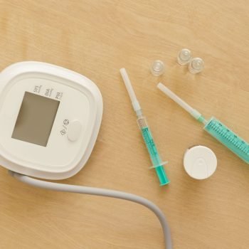 Flat lay of medical equipment including a sphygmomanometer and syringes on a wooden surface.