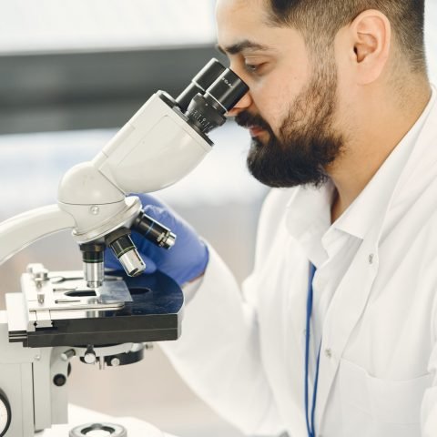 A scientist focused on examining samples through a microscope in a laboratory setting, showcasing scientific research and discovery.
